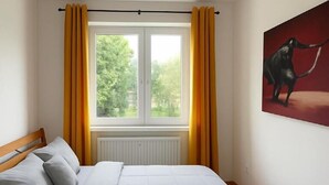 A bedroom with a bed, a window with curtains, a radiator, and a painting on the wall. - Large Family Apartment for 7 - Central BA (Bratislava)