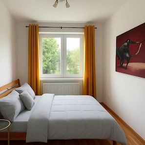 A bedroom with a bed, a window with curtains, a radiator, and a painting on the wall.