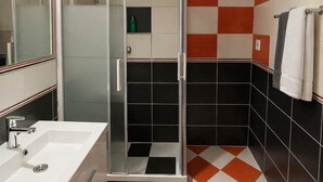 A bathroom with a glass shower enclosure, a white sink, and a checkered floor pattern. - Large Family Apartment for 7 - Central BA (Bratislava)