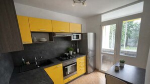A modern kitchen with yellow cabinets, a stainless steel refrigerator, and a window providing natural light. - Large Family Apartment for 7 - Central BA (Bratislava)