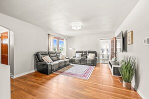 A spacious living room with hardwood flooring, a black leather sofa, a matching loveseat, and a large area rug. - Roadmap Lodging: 3BR Near Columbus Regional Health (Columbus)