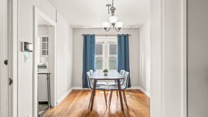 A dining room with a wooden table and chairs, a chandelier, and a view through a window with blue curtains. - Roadmap Lodging: Near Columbus Regional Health, 3BR Monthly, Pet OK (Columbus)