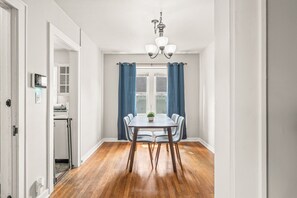 Ein Esszimmer mit Holztisch und -stühlen, einer Chandelier und Blick durch ein Fenster mit blauen Vorhängen.