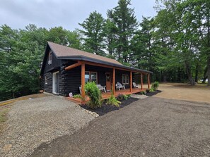 Eine Blockhütte mit Veranda, zwei Stühlen und einem Schotterweg.
