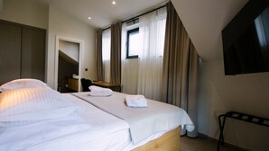 Une chambre d’hôtel avec un lit, un bureau, une chaise, une télévision et une fenêtre avec des rideaux.