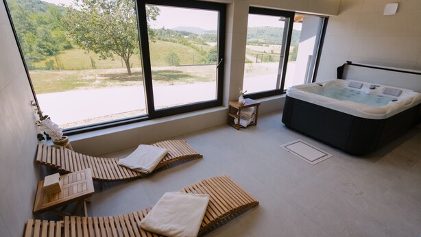 Une salle de spa dotée d’un jacuzzi, de chaises longues en bois et offrant une vue sur un paysage verdoyant grâce à de grandes fenêtres.