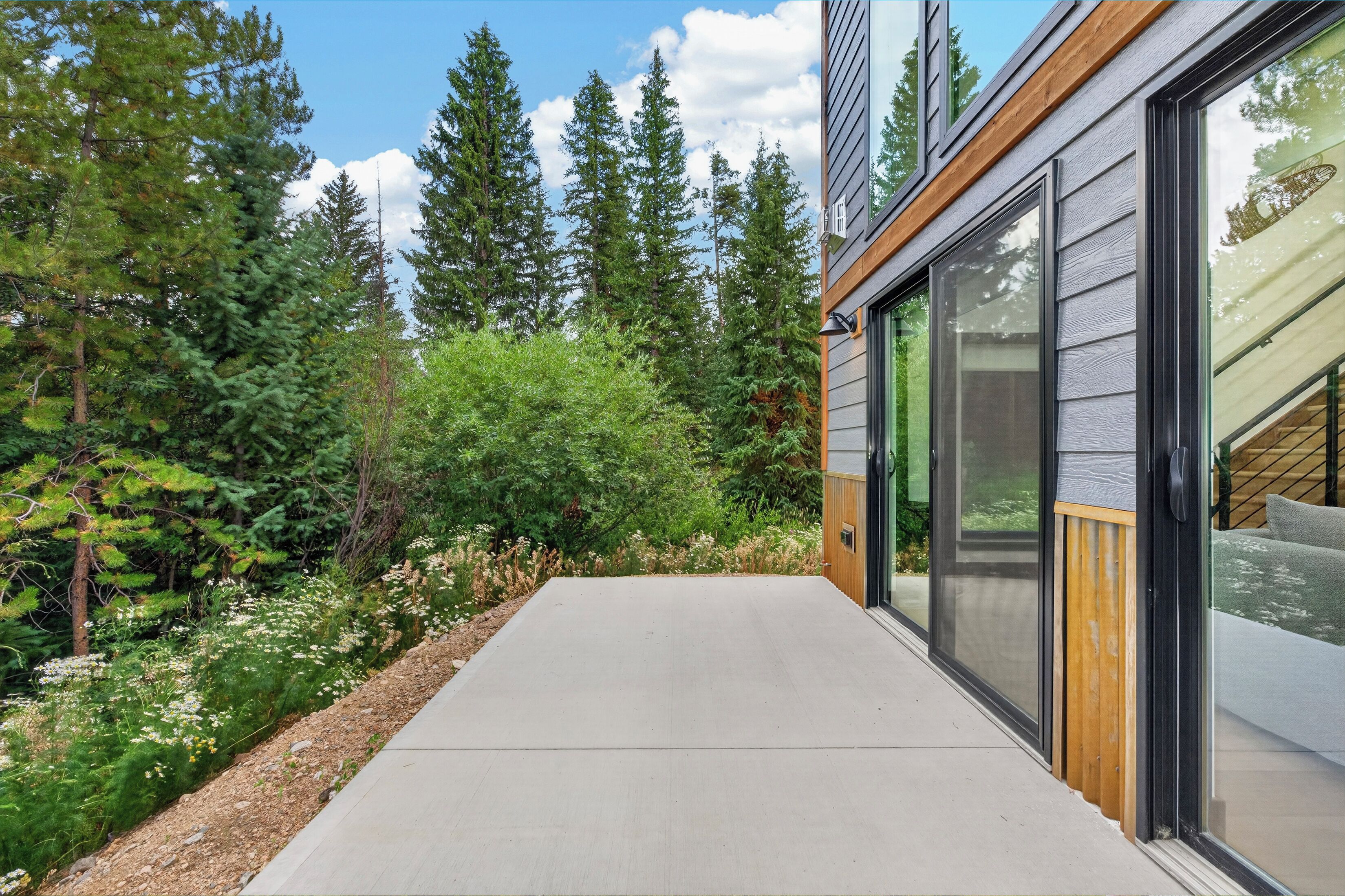 A modern building with large glass windows, a concrete pathway, and a forested area.