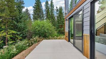 A modern building with large glass windows, a concrete pathway, and a forested area.