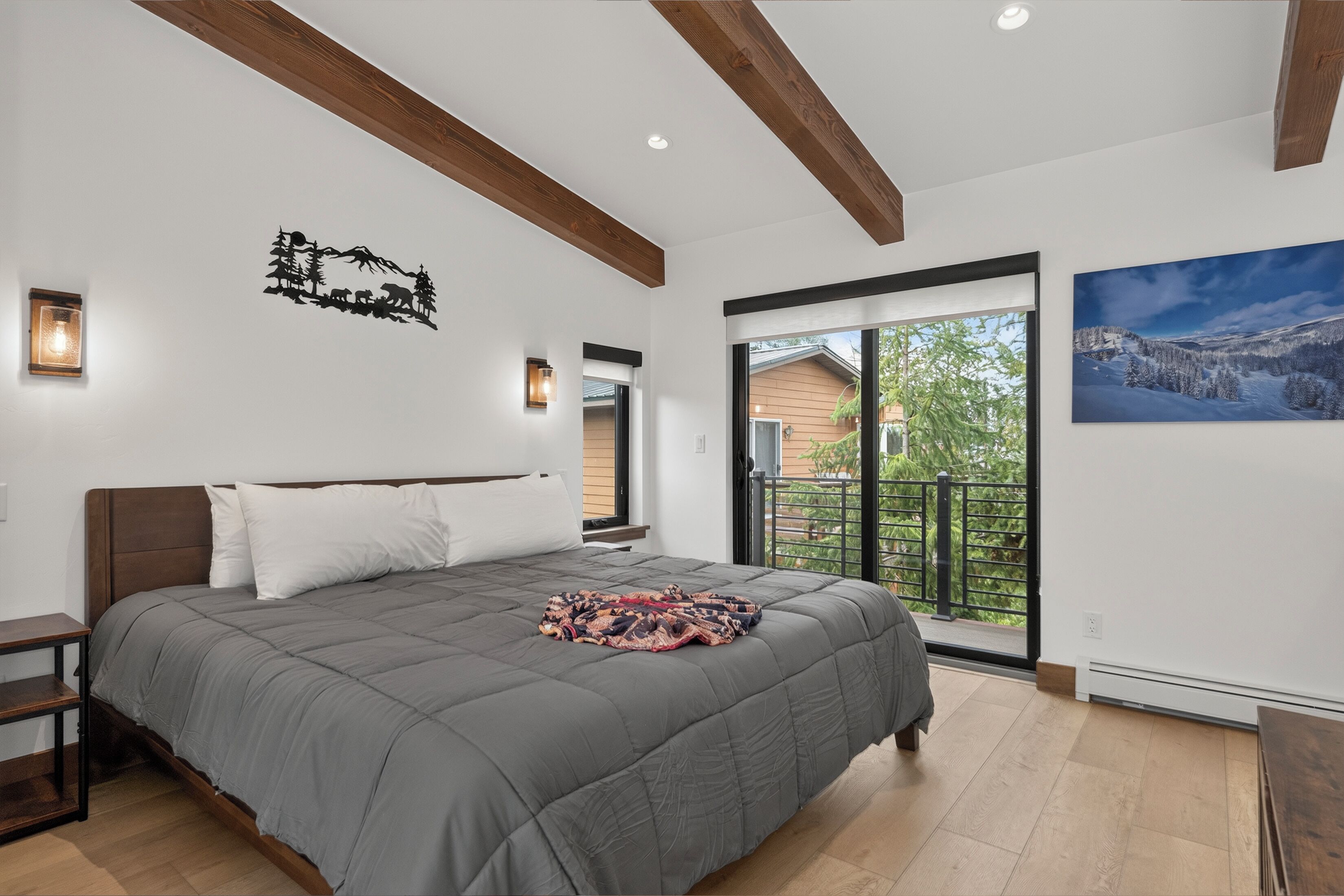 A bedroom with a large bed, wooden beams, a window with a view, and wall-mounted lights.