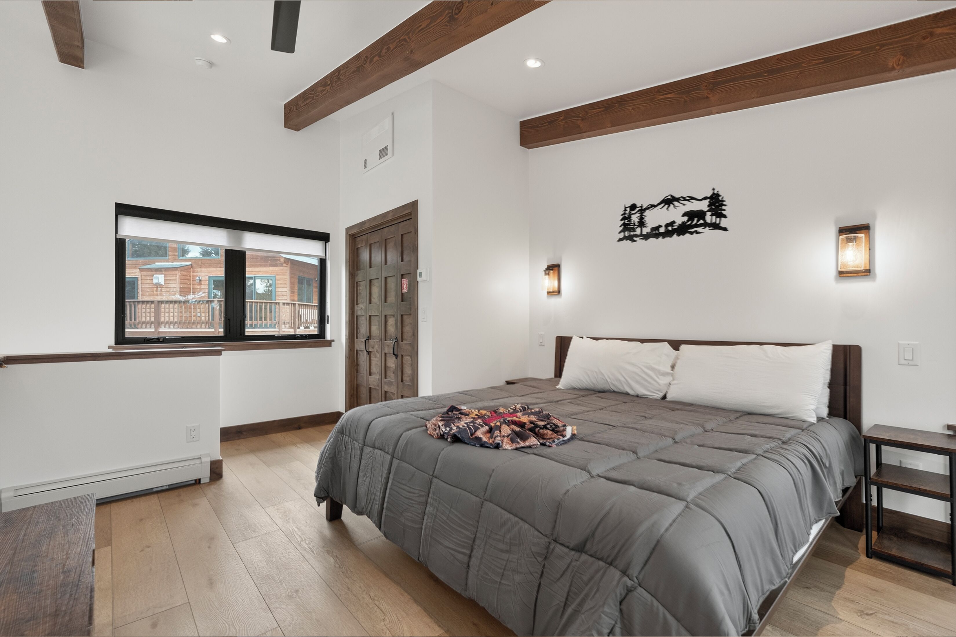 Une chambre à coucher avec un grand lit, des poutres en bois, une fenêtre avec vue et un luminaire fixé au mur.