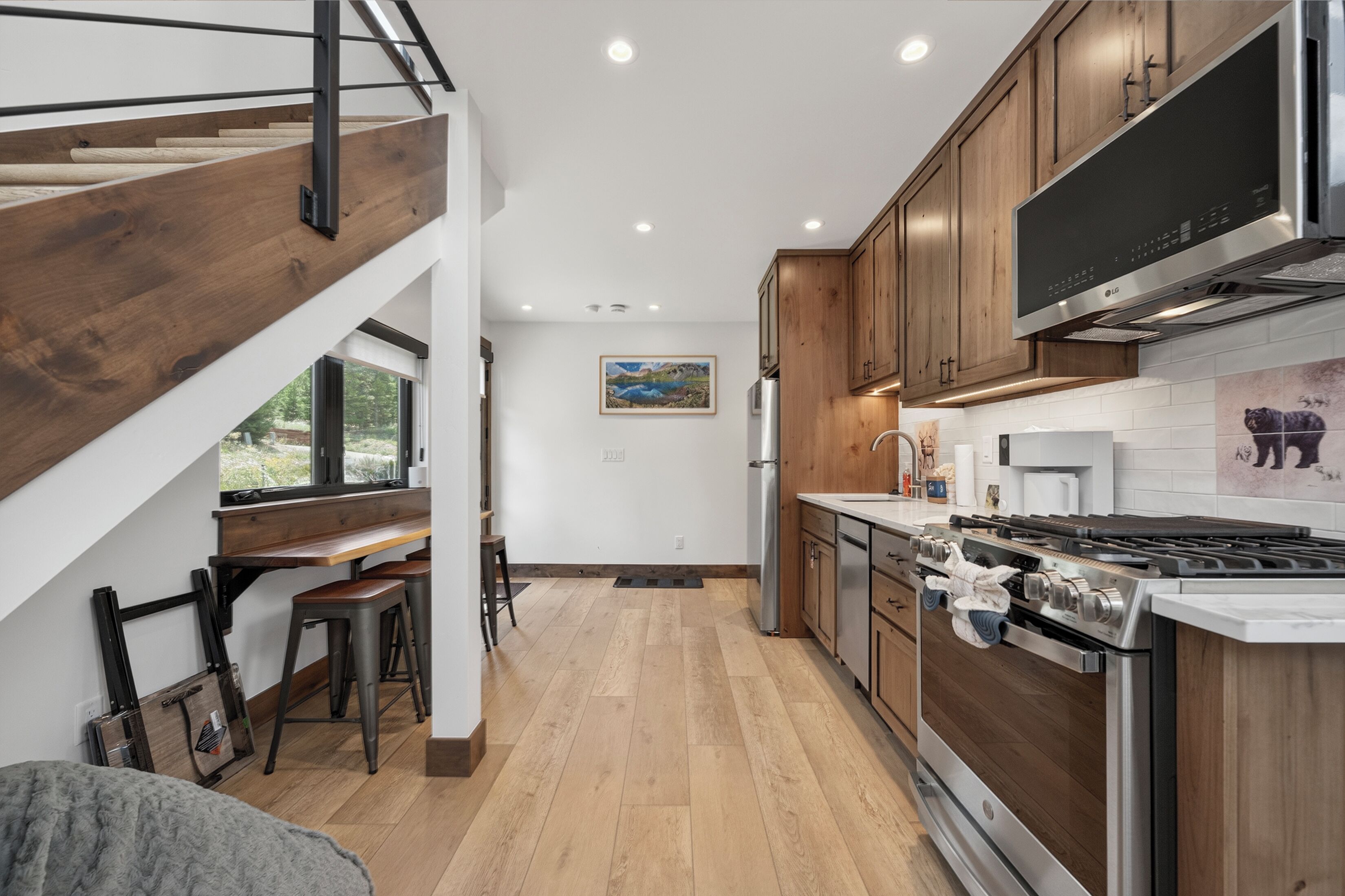 A modern kitchen with wooden cabinets, a stainless steel stove, and a dining area with a bench and stools.