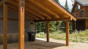 A covered outdoor area with wooden beams and a gravel ground, a trash bin, and a building in the background.