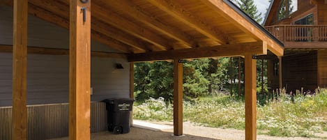 Ein überdachter Außenbereich mit Holzbalken und Kiesboden, ein Mülleimer und ein Gebäude im Hintergrund.