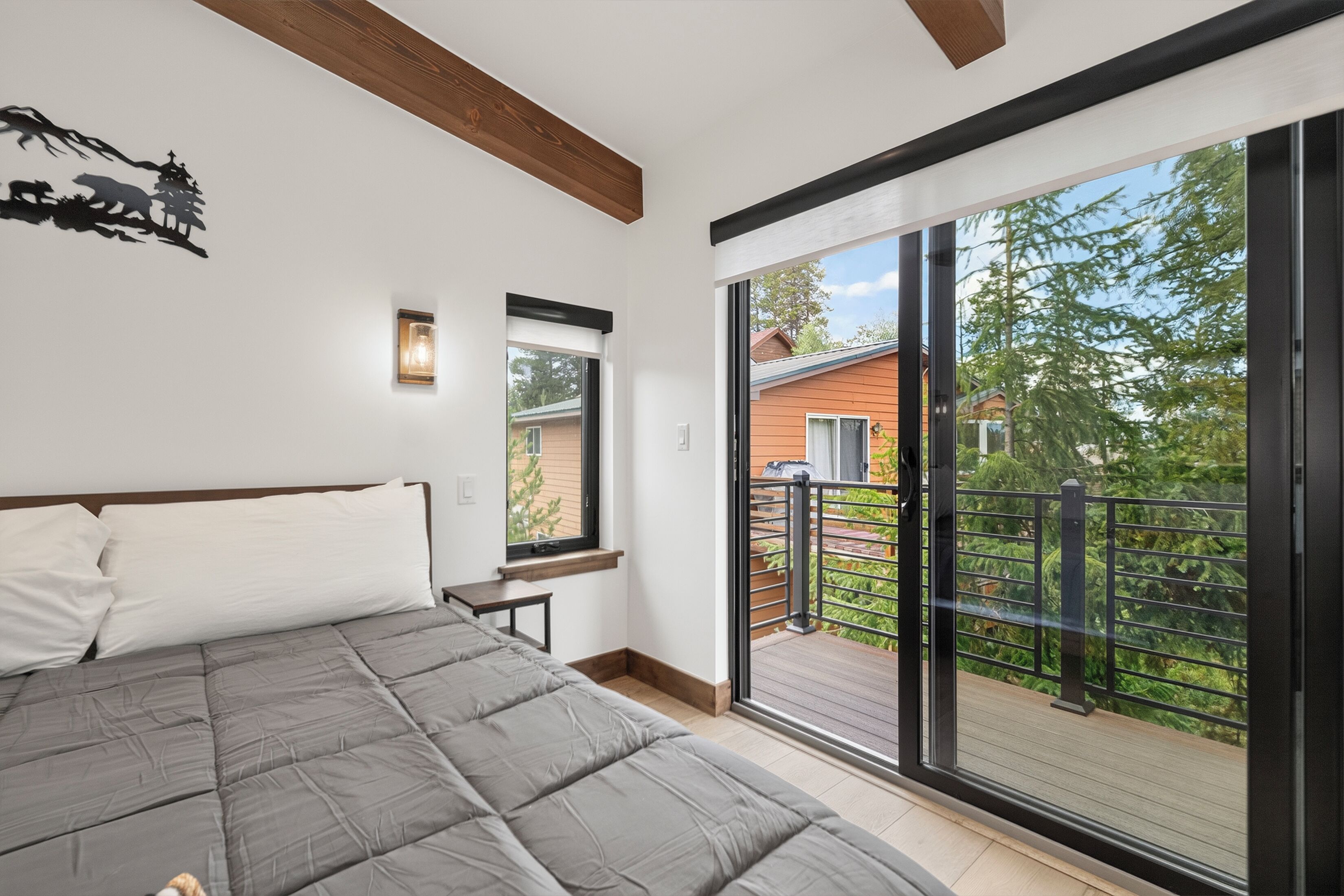 A bedroom with a large bed, a window, and a balcony with a view of a house and trees.