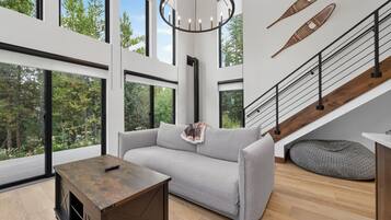 A modern living room with a grey sofa, a wooden coffee table, and a staircase with a wooden finish.