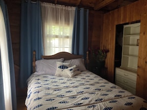 A wooden room with a bed, a dresser, and a window with curtains.