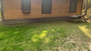 Una cabaña de madera con techo de paja, una mesa de picnic y un banco.