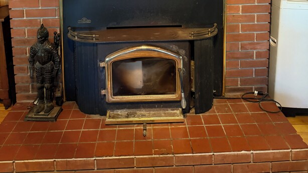 Una chimenea de ladrillo con estructura metálica, una pequeña estatua a la izquierda y un electrodoméstico blanco a la derecha.