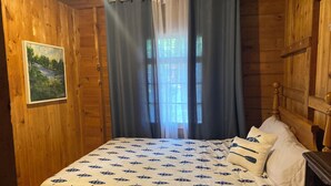 Una habitación de madera con cama, un cuadro en la pared y una ventana con cortinas.