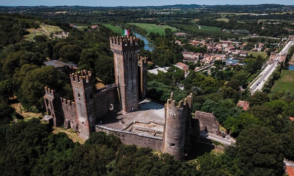 Een historisch kasteel met meerdere torens, omgeven door weelderige begroeiing en een klein stadje op de achtergrond.