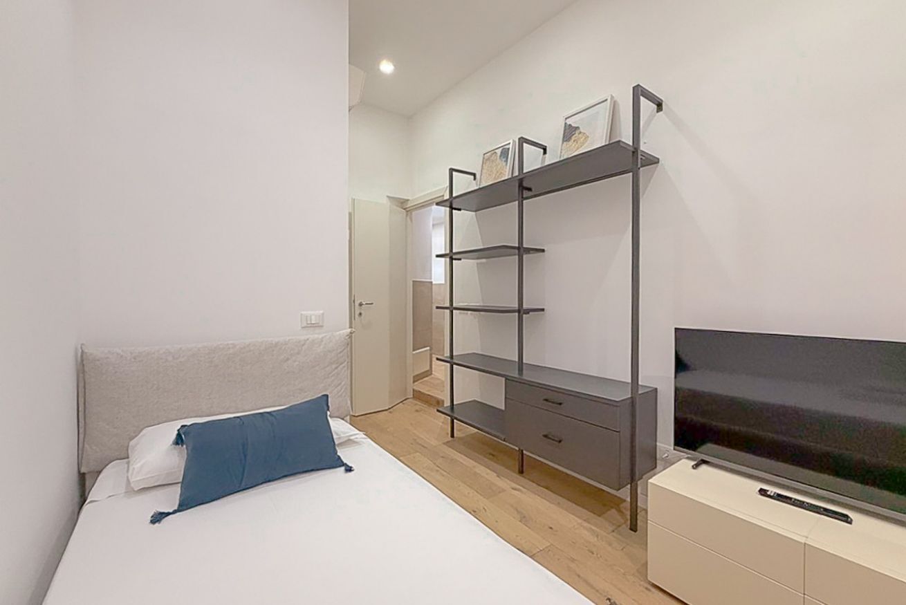 A bedroom with a bed, a TV on a stand, and a shelving unit against the wall.