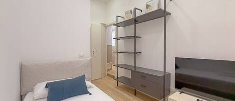 A bedroom with a bed, a TV on a stand, and a shelving unit against the wall.