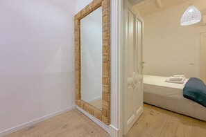 Ein Zimmer mit einem spiegelnden Holzbettrahmen, einem Bett mit weißer Matratze und blauer Bettwäsche sowie einer hängenden Leuchte.
