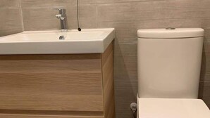 Ein Badezimmer mit einem Holzkosmetikschrank, einem weißen Waschbecken und einer weißen Toilette.