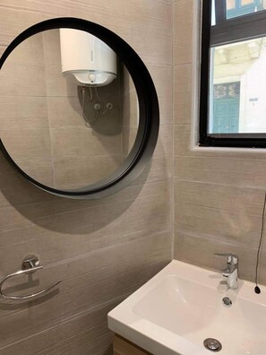 Ein Badezimmer mit rundem Spiegel, Waschbecken und Fenster.