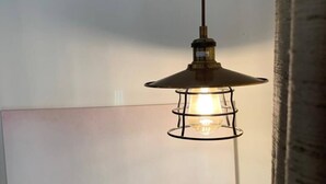 Eine Pendelleuchte mit Metallrahmen und konischem Schirm, die an der Decke hängt.