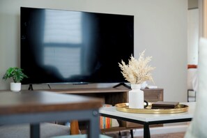 A living room with a flat-screen TV, a white vase with dried flowers, and a tray with books. - Roadmap Lodging: Single-Level 3BR, Garage, Yard (Columbus)