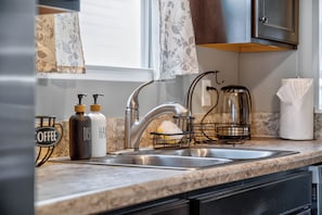 A kitchen with a stainless steel sink, a coffee dispenser, and a dish soap bottle. - Roadmap Lodging: Single-Level 3BR, Garage, Yard (Columbus)