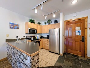 Een moderne keuken met een centraal eiland, roestvrijstalen apparatuur, houten kasten en een accentmuur van steen.