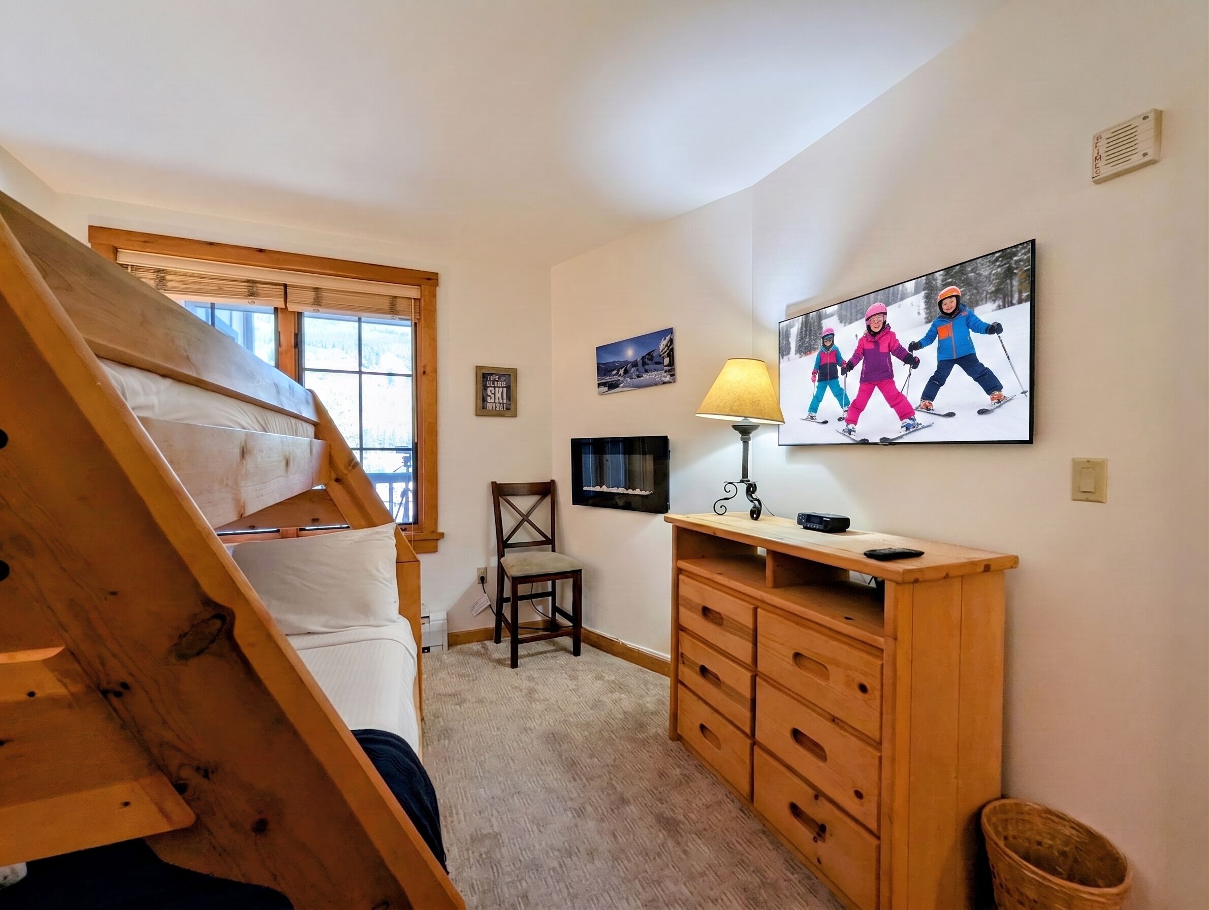 Een slaapkamer met een stapelbed, een bureau met een lamp, een televisie en een lijst met skiërs.