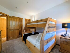 Een stapelbed met houten frame, een nachtkastje met lamp en een kledingkast.