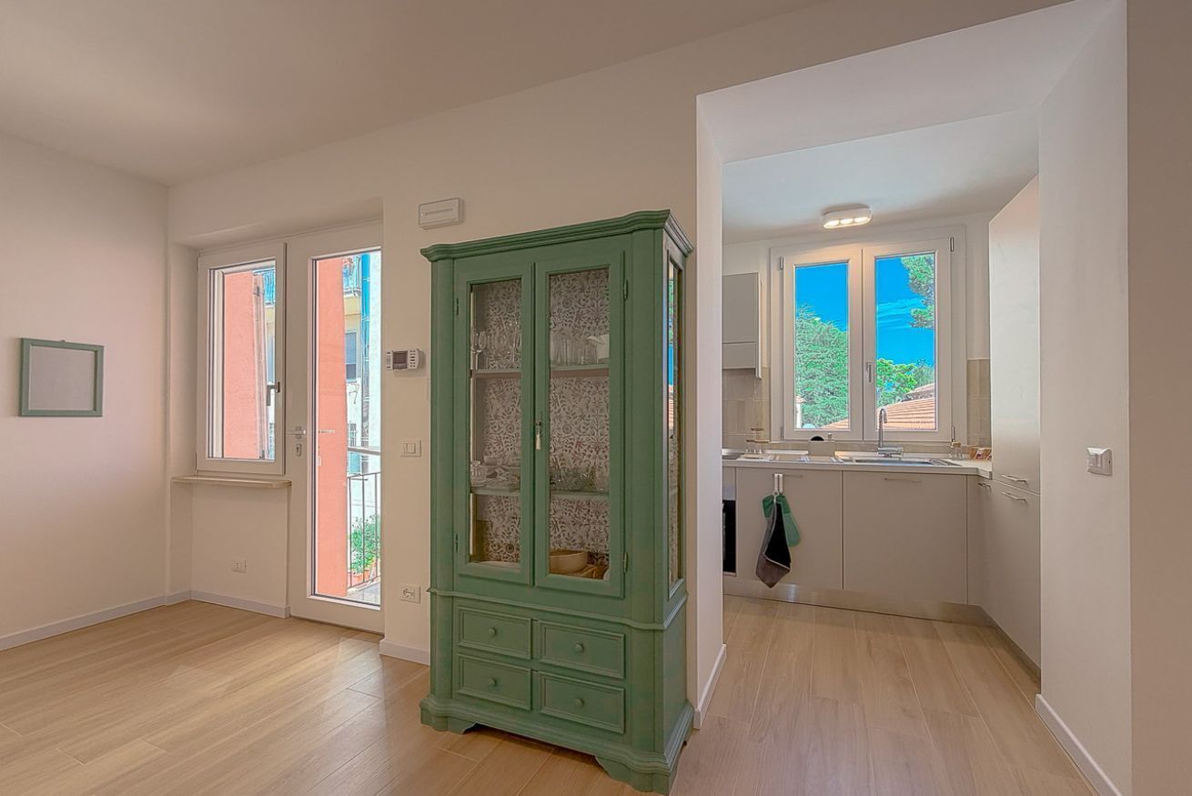 A room with a green cabinet, a kitchen area, and a door leading to an outdoor space.