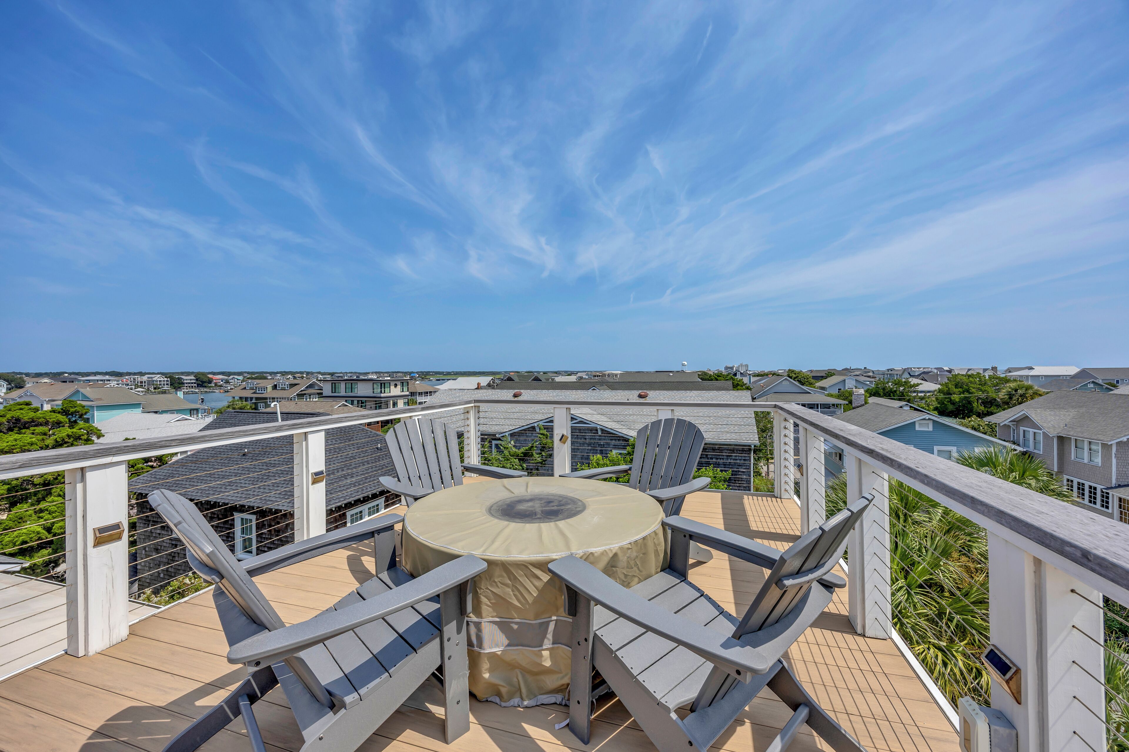 A rooftop terrace with a round table and two chairs, overlooking a residential area with houses and a body of water.