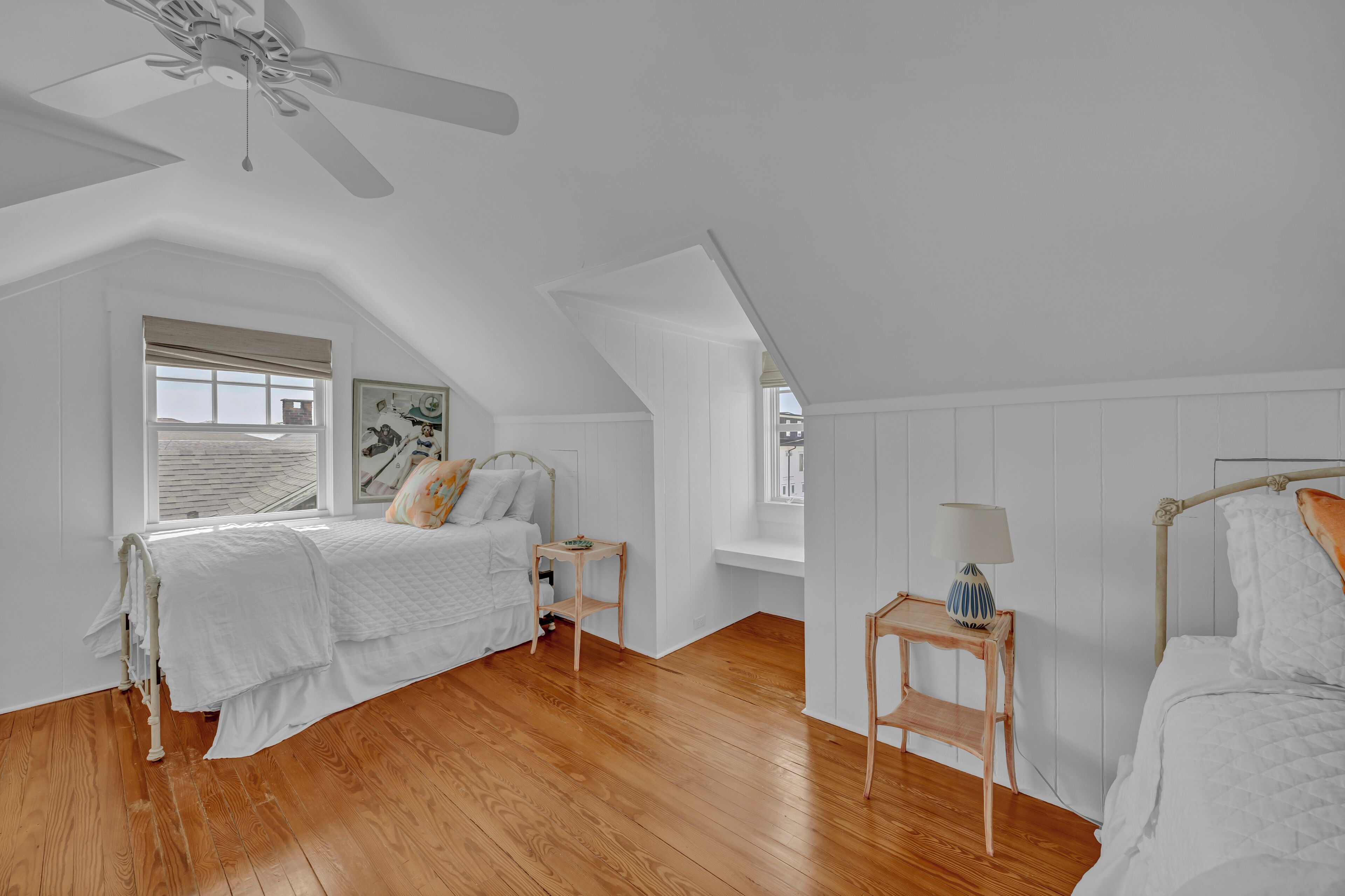 Une chambre à coucher avec un plafond en pente, un lit, une table de chevet, une lampe et une fenêtre avec des stores.
