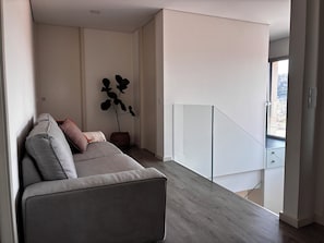Uma sala de estar moderna com um sofá cinzento, uma planta em vaso e uma escadaria que dá para uma varanda externa.
