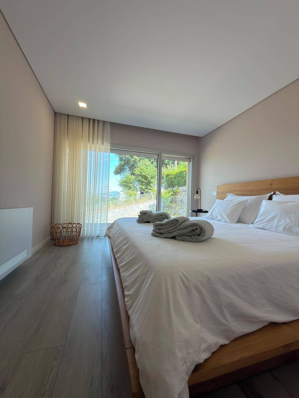 Hotelkamer met groot bed, nachtkastje, lamp, rieten mand en uitzicht op de omgeving.