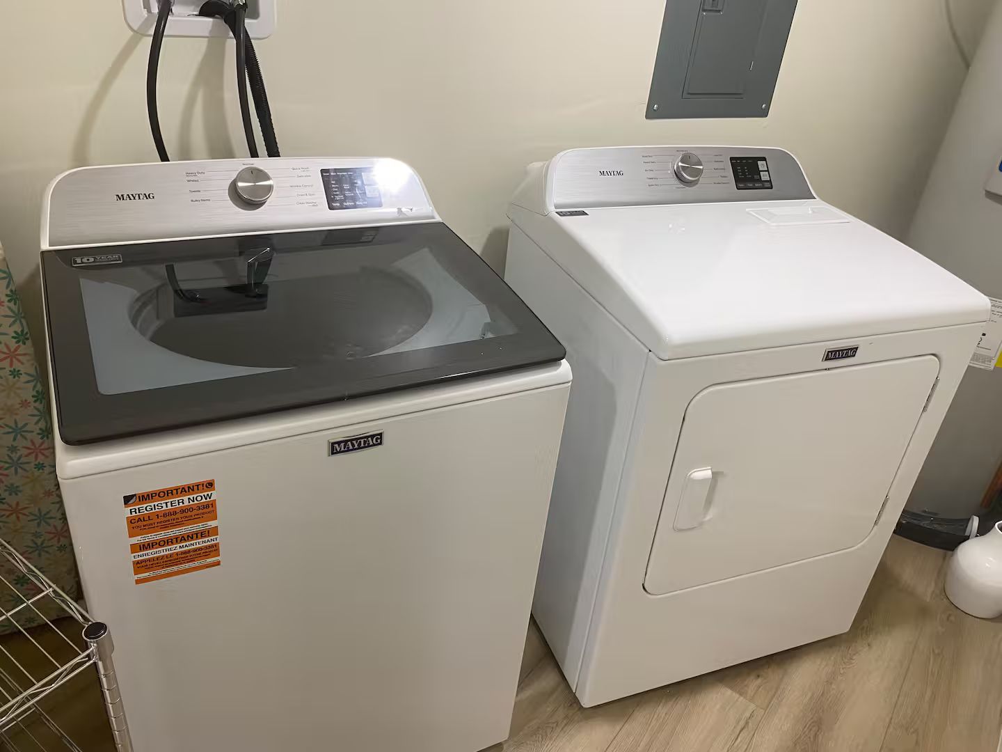 Two Maytag washing machines in a laundry room with a power outlet and a wall-mounted electrical box.
