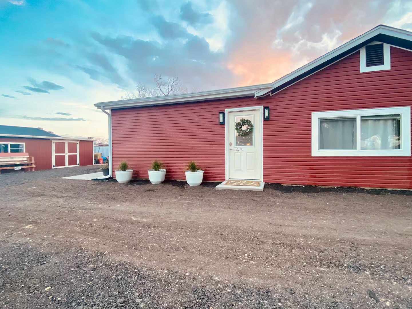 A red single-story house with a white door, a small window, and three potted plants in front.