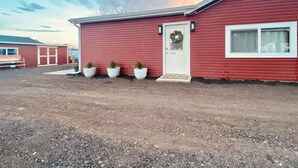 Una casa vermella d'un pis amb una porta blanca, una finestra petita i tres plantes en testos al davant.
