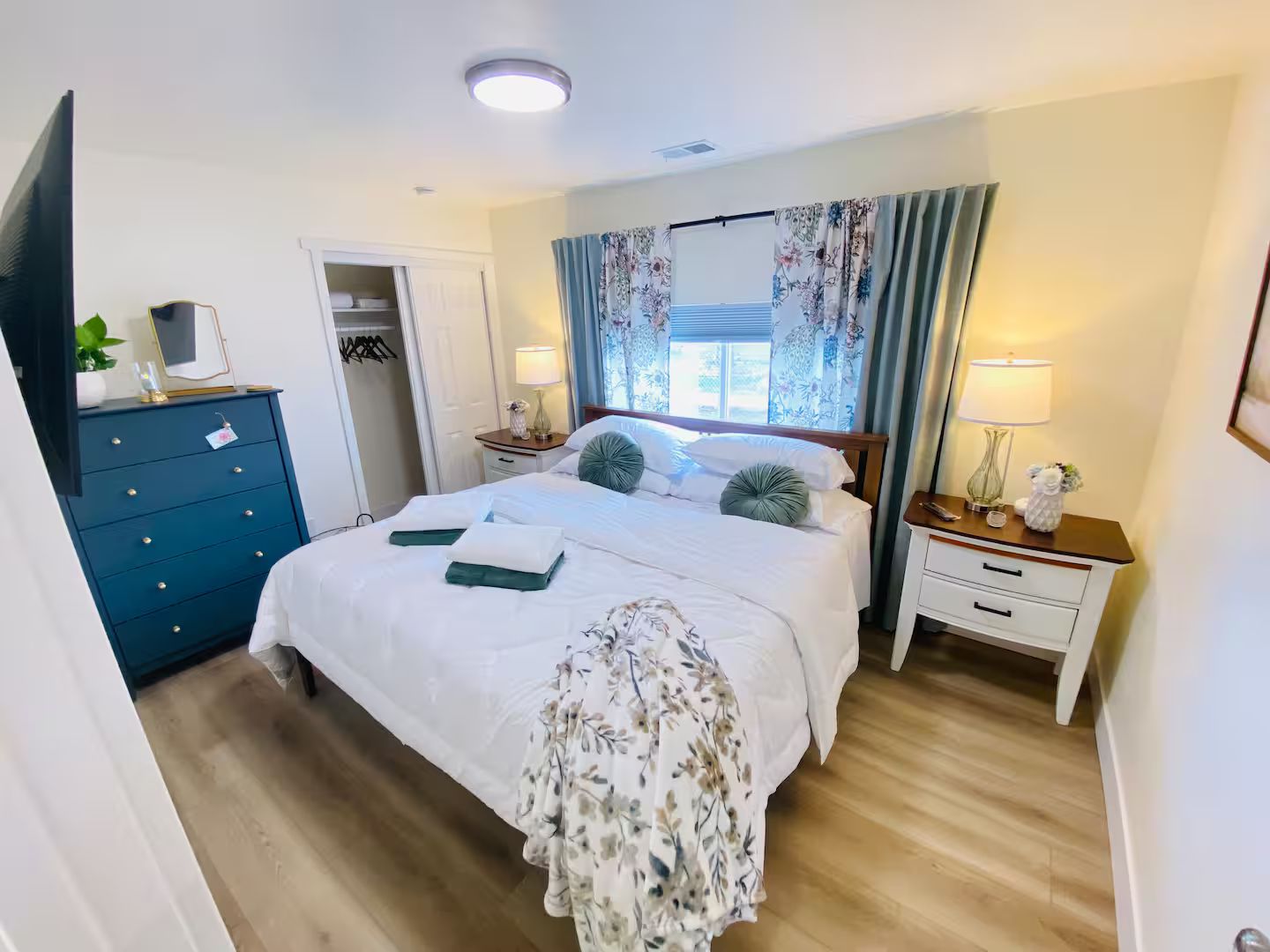 A hotel room with a bed, bedside tables, a wardrobe, and a window with curtains.