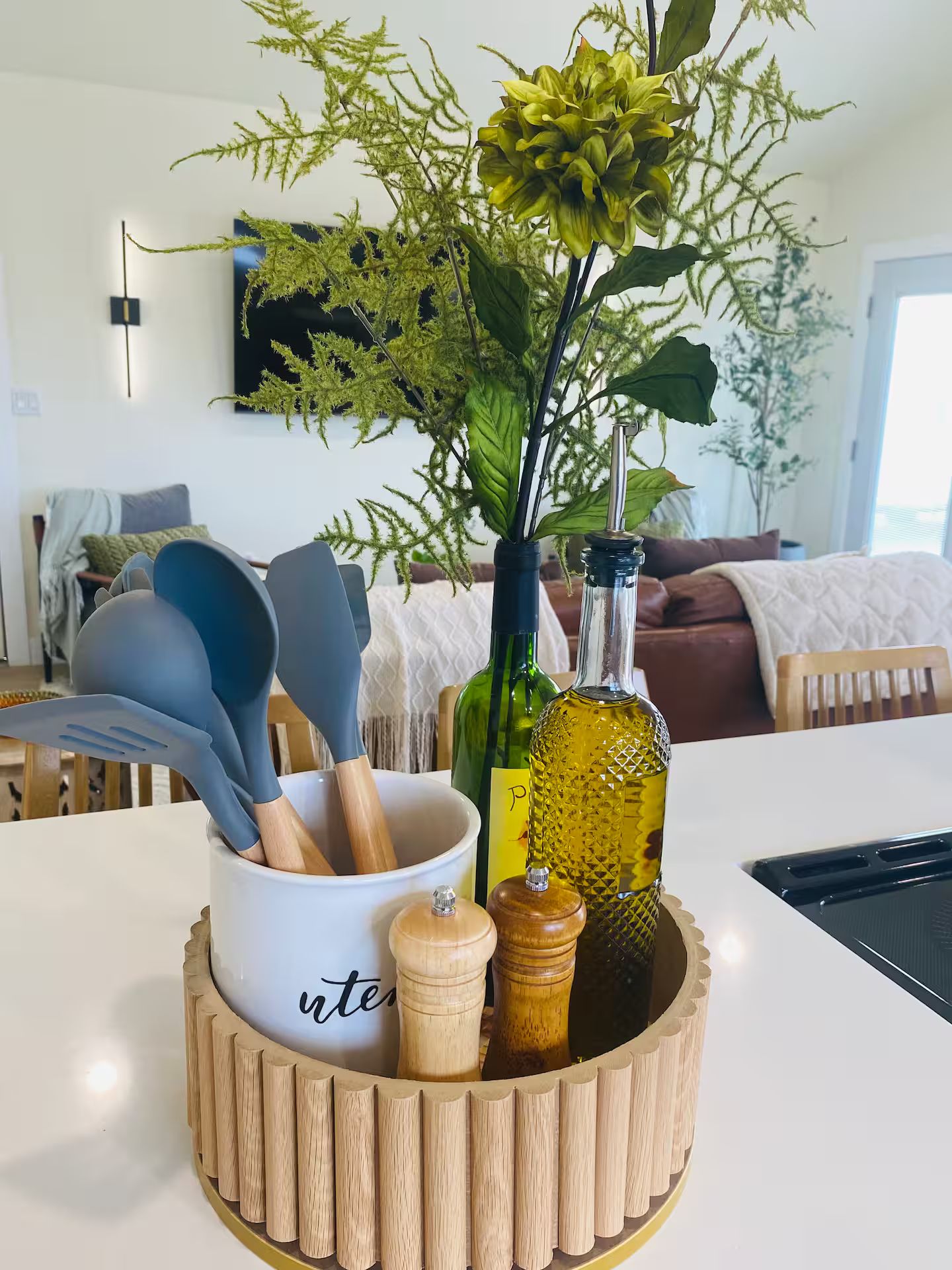 A kitchen counter with a wooden bowl containing kitchen utensils, a bottle, and a plant.