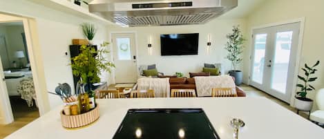 A modern kitchen with an induction cooktop, a stainless steel range hood, and a dining area with a sofa and chairs.