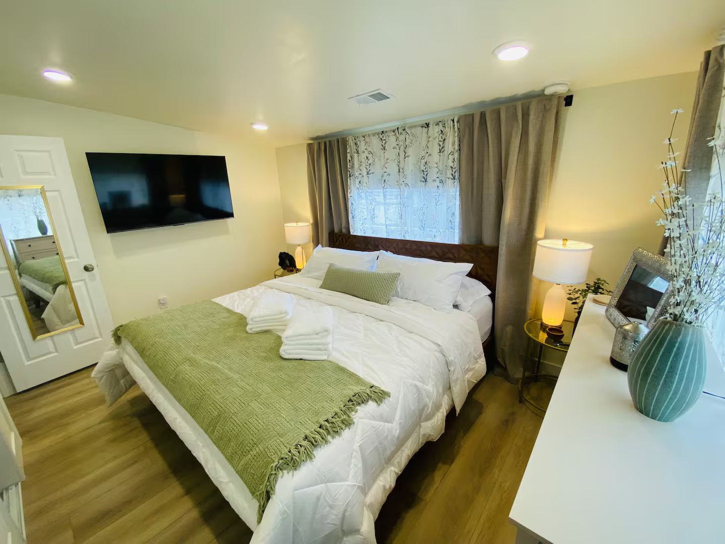 Une chambre d’hôtel avec un lit, une télévision, un bureau avec une lampe et un vase rempli de fleurs.
