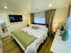 A hotel room with a bed, a TV, a desk with a lamp, and a vase with flowers.