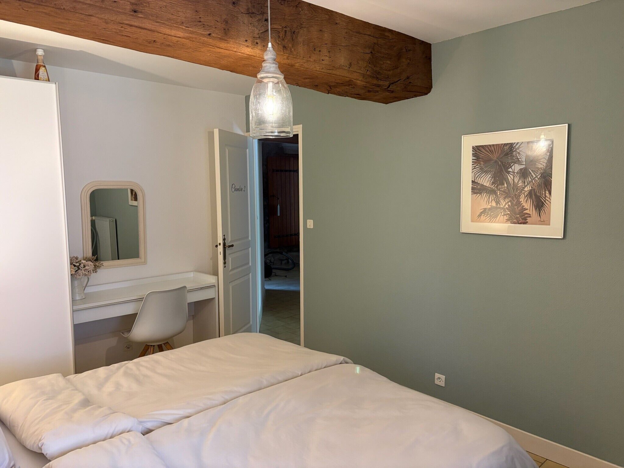 Ein Schlafzimmer mit einem Bett, einem Schreibtisch, einem Stuhl, einem Spiegel, einer Pendelleuchte und einem gerahmten Bild an der Wand.