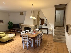 A dining area with a wooden table and chairs, a fireplace, and a television in the background.